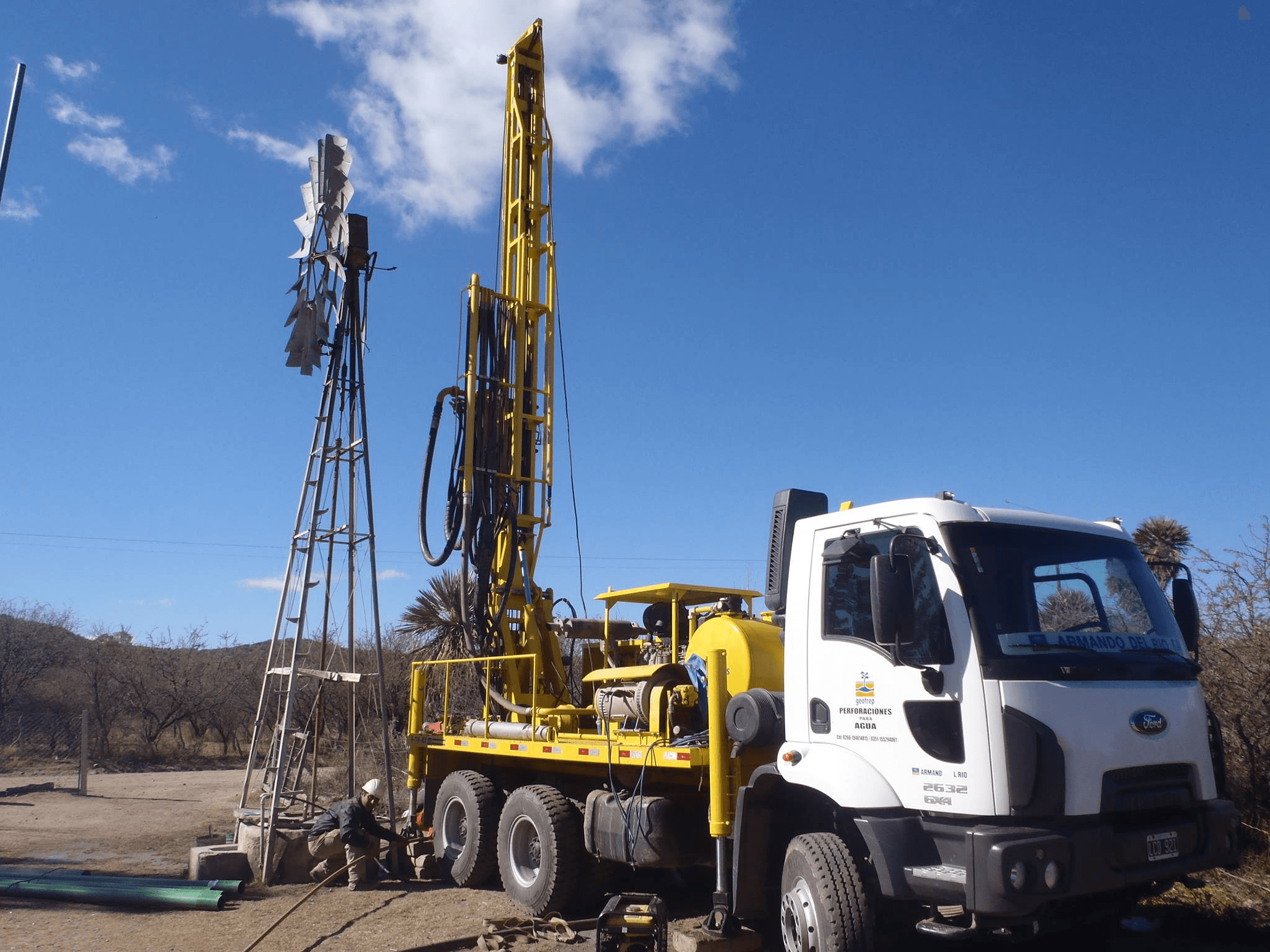 Camión perforador de Geotrep trabajando junto a un molino en el campo